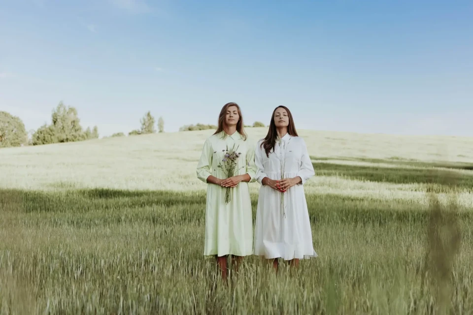 Two models in light-colored ELiZA dresses standing in a meadow